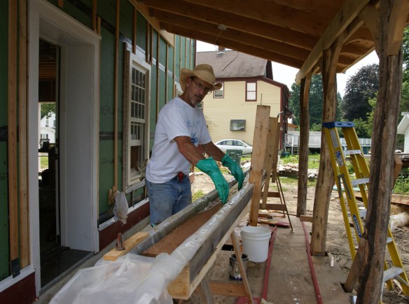 Andy dipping red cedar tongue and groove siding board in trough of Penofin stain